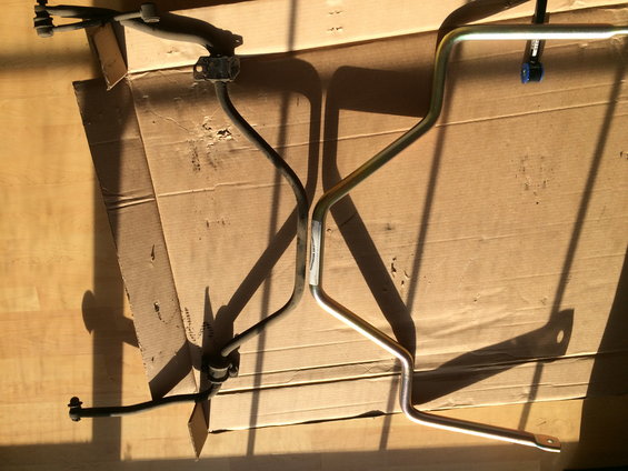 Two sway bars, one black and one silver, laid out on cardboard