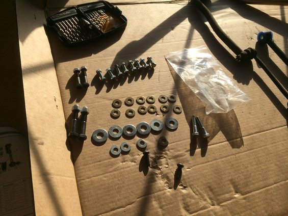 Sway bar links, bolts, washers, and drill bits laid out on cardboard