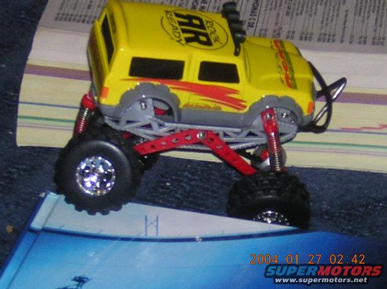 Yellow toy monster truck with red suspension and large tires, seen from a 3/4 front angle