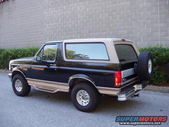 Black Ford Bronco with tan top and spare tire on back, parked on asphalt