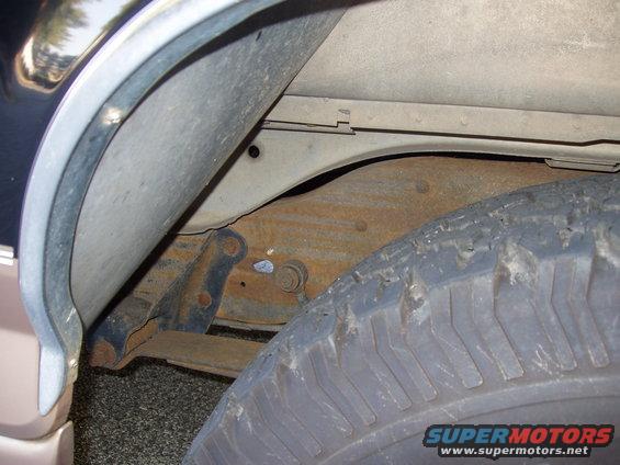 Close-up of a vehicle's rear wheel well showing the tire, suspension arm, and rusted frame components