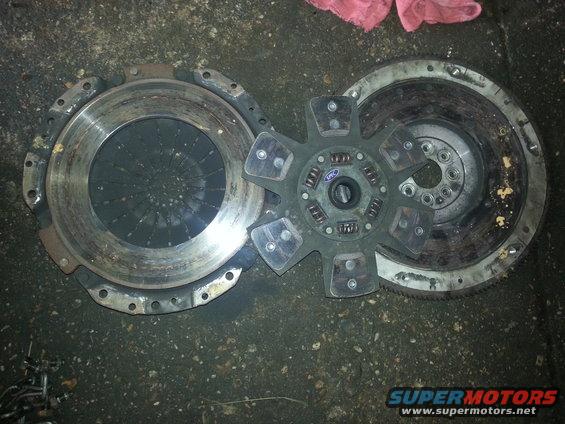 Clutch disc, pressure plate, and flywheel assembly on a dark, dirty surface