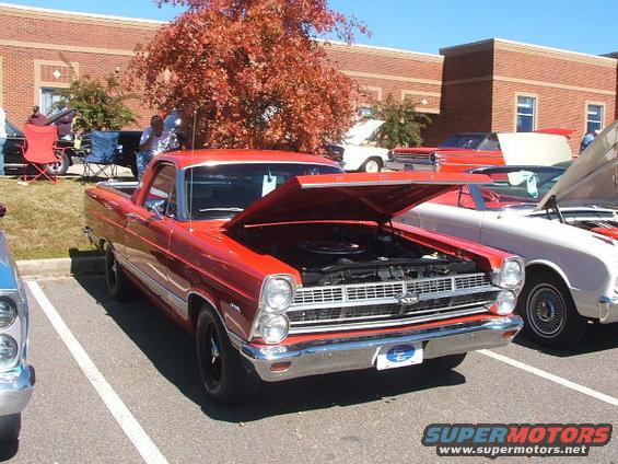 Red 1968 Ford Ranchero parked at a car show, hood open, showing the engine