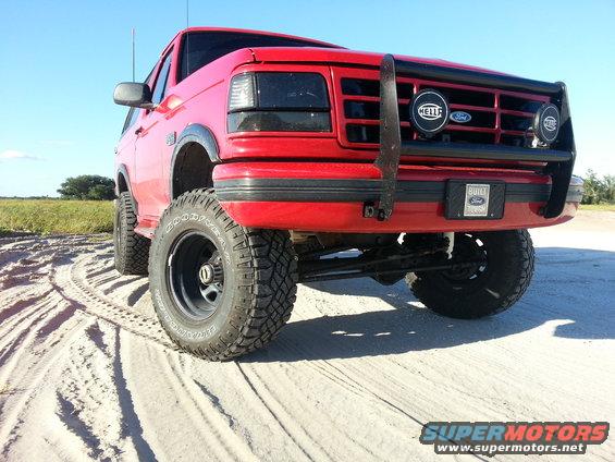 Red Ford Bronco with lifted suspension and off-road tires on sandy terrain