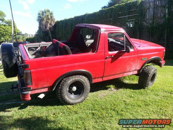 Red 1995 Ford Bronco with removable top and spare tire on the back, seen from the rear three-quarter view