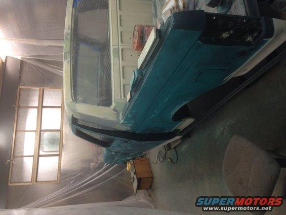 Vehicle body being prepped for paint, covered in plastic sheeting inside a booth