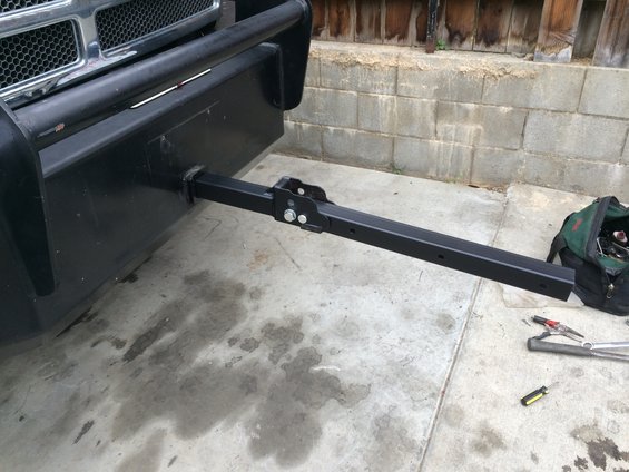 Front of a truck with a hitch receiver extended. Tools and a bag are on the ground nearby