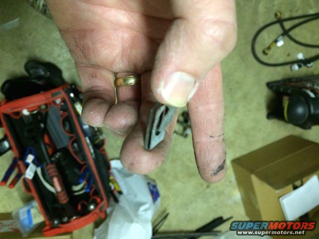 Hand holding a gray windshield wiper part. Toolbox and boxes in background