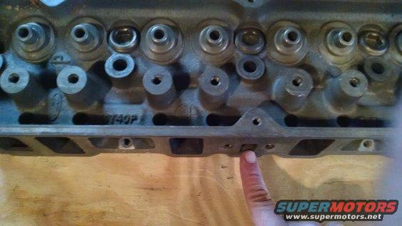 Engine cylinder head with visible text '140P' and a finger pointing to a bolt hole