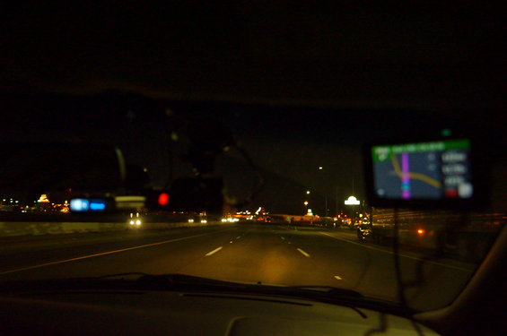 View from inside a car driving on a highway at night, with a GPS device mounted on the dashboard
