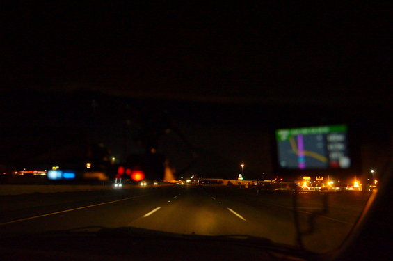 Dashboard view at night with GPS screen showing a route, highway lights in distance