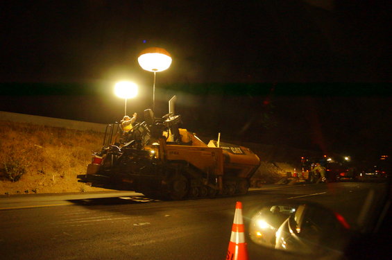 Yellow asphalt paver with CAT logo at night, illuminated by large lights