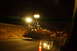 2003 Ford Taurus - Road construction equipment operates at night, illuminated by bright lights, with a car's reflection visible in the foreground.