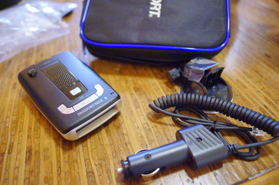 Passport Max 4 radar detector with coiled cord, car charger, and suction cup mount on wooden table