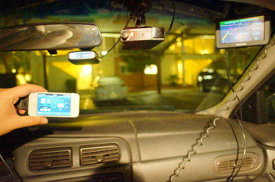 Dashboard interior with a hand holding a smartphone, a Garmin GPS, and a dashcam