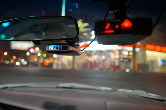 Radar detector and rearview mirror mounted on windshield at night, with blurred city lights in background