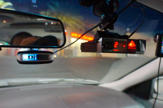 Radar detector with red digital display and GPS device with blue display mounted on windshield