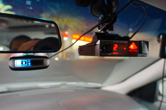 Radar detector and dashcam mounted on windshield, with rearview mirror visible