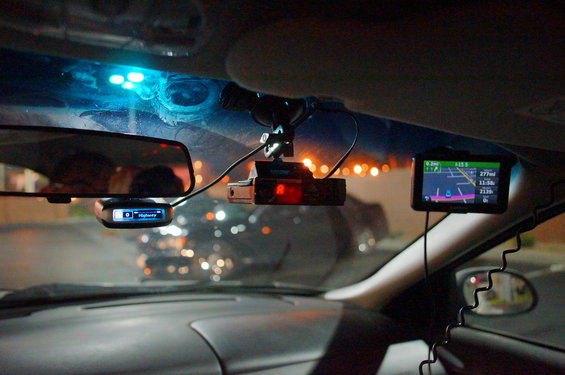 Car interior showing radar detector, GPS, and rearview mirror with lights reflecting on windshield