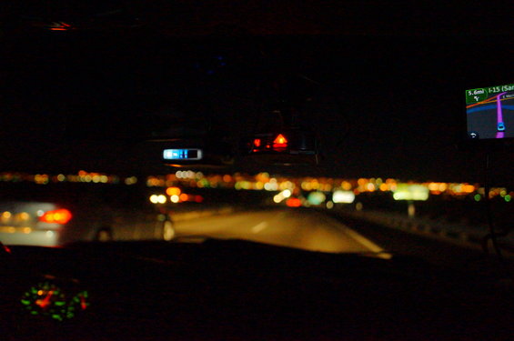 Driving on a highway at night, with city lights in the distance and a GPS screen showing the route