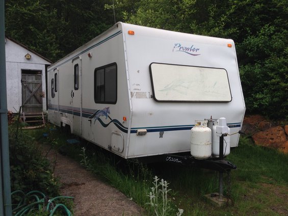 White travel trailer with 'Prowler' logo parked next to a shed