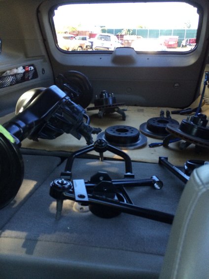 Various car suspension parts, including control arms and brake rotors, are stored inside a vehicle