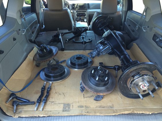 Various car parts including axles, brake rotors, and suspension components laid out on cardboard in the cargo area of an SUV