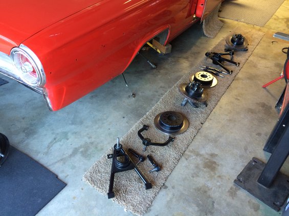Red 1964 Ford Fairlane side view, showing disassembled front suspension components laid out on a rug