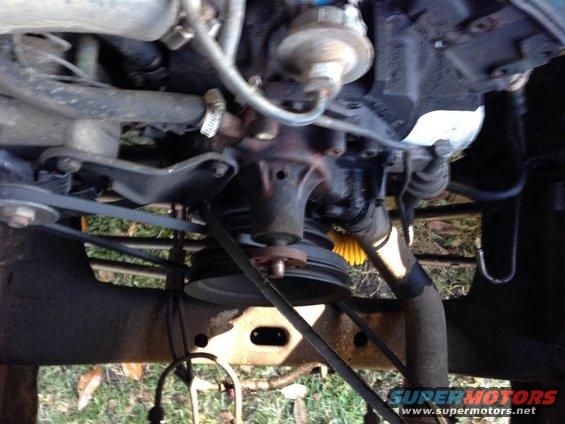 Engine water pump with belts and pulleys visible. Some hoses and engine components are also in the frame