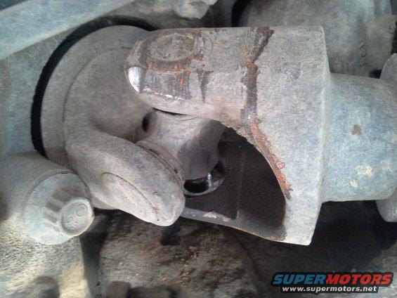 Driveshaft universal joint with rust and damage. A black rubber boot is visible