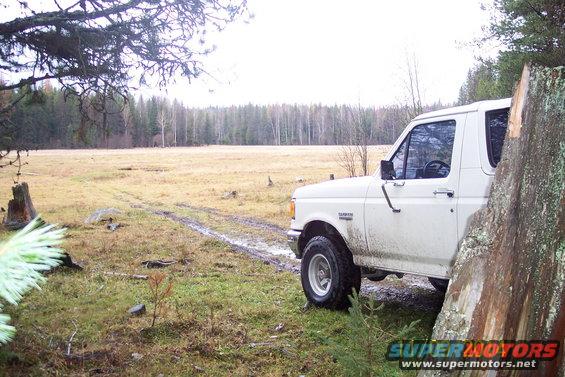 1990 Ford Bronco parked on a muddy track in a field with trees in the background