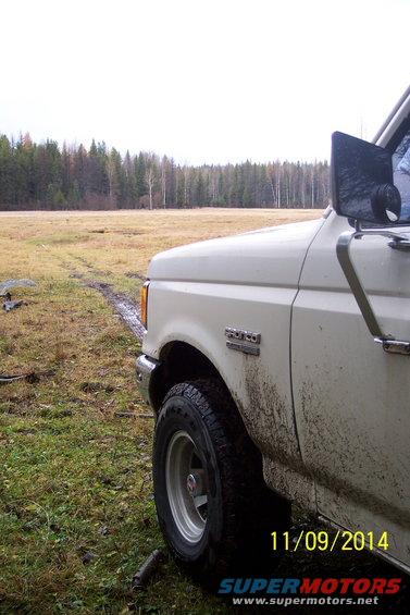 White Ford Bronco, mud-splattered, parked in a grassy field with trees in the background. Date stamp reads 11/09/2014