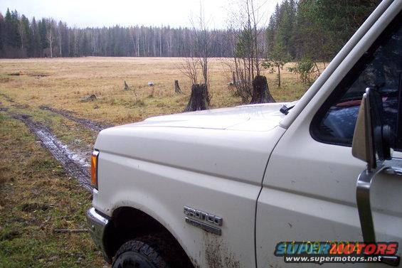 White Ford Bronco with "BRONCO" badge, seen from the front-right in a muddy field