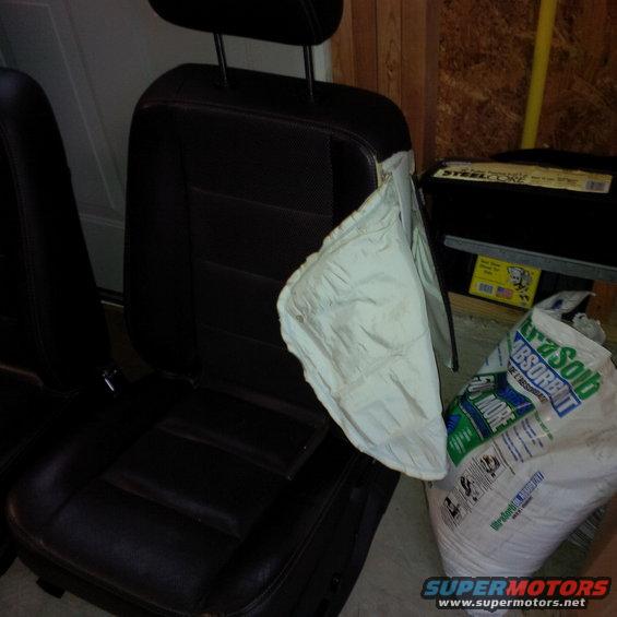 Car seat with a deployed airbag hanging out, next to a bag of absorbent material