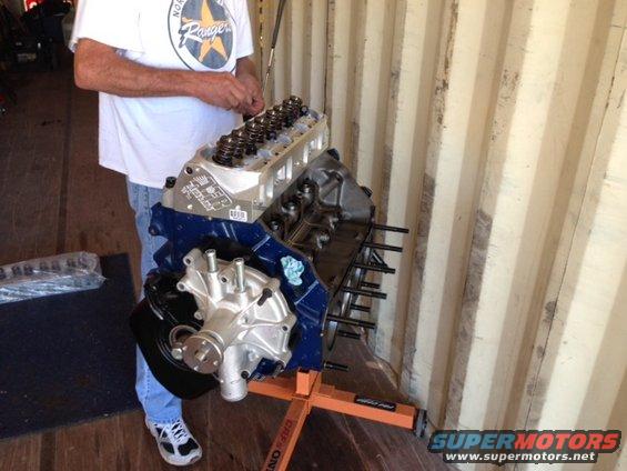 Engine on an orange stand, with a person in a white t-shirt and blue jeans nearby