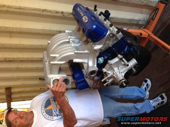 Man holding a supercharged Ford V8 engine on an orange engine stand