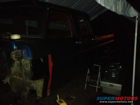 Truck cab and front fender area visible under a tarp, with tools and a ladder nearby