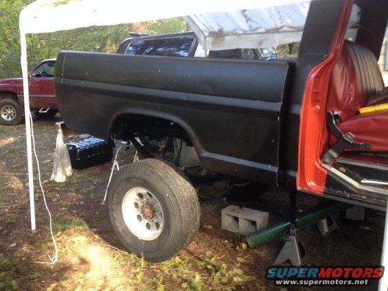 1973 Ford F-Series truck with black bed and red cab, lifted on jack stands with a new fuel tank visible