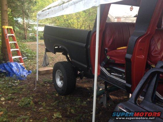 Black Ford F-Series truck with red interior, lifted, on jack stands, under a canopy