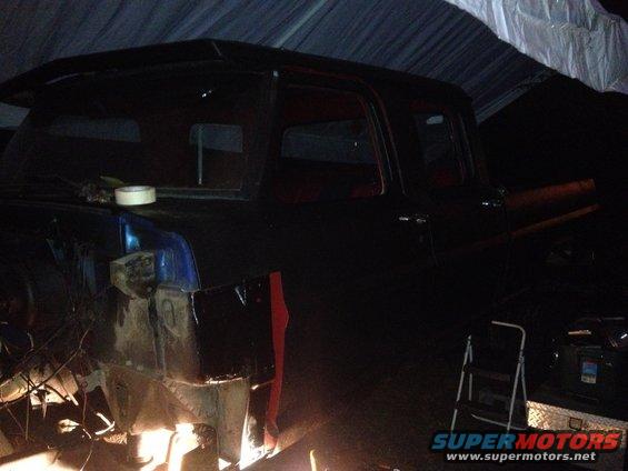 Side view of a dark pickup truck undergoing repairs, showing exposed metal and red trim