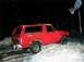 1990 Ford Bronco - A red SUV is partially buried in snow, with a basketball hoop visible in the dark, snowy background.