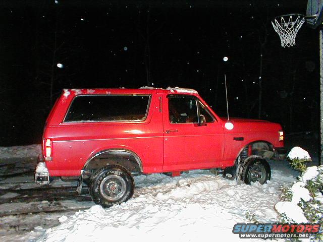 Red 1990 Ford Bronco in snow, side view, lifted suspension