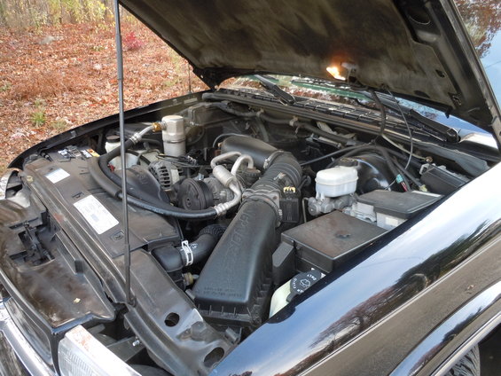 Engine bay of a black vehicle with hood open, showing engine components and wiring
