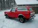 1990 Ford Bronco - A red 1990 Ford Bronco is partially buried in snow, parked in front of a house with icicles hanging from the roof.