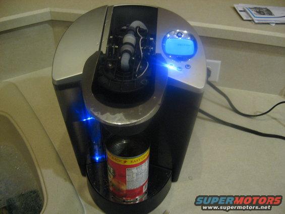Black and silver coffee maker with blue lights, holding a can of food