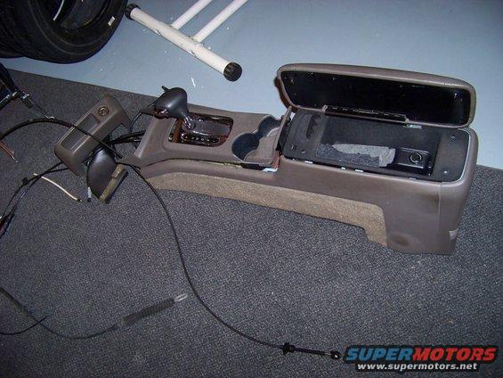 Car's center console removed, showing the shifter, cup holders, and open storage compartment