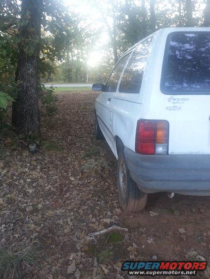 1991 Ford Festiva parked on a dirt path with trees and sun glare
