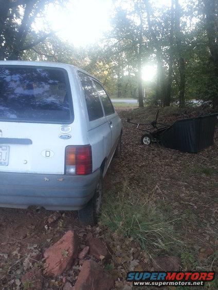 1991 Ford Festiva hatchback, white, rear view, parked on dirt with trees and a trailer