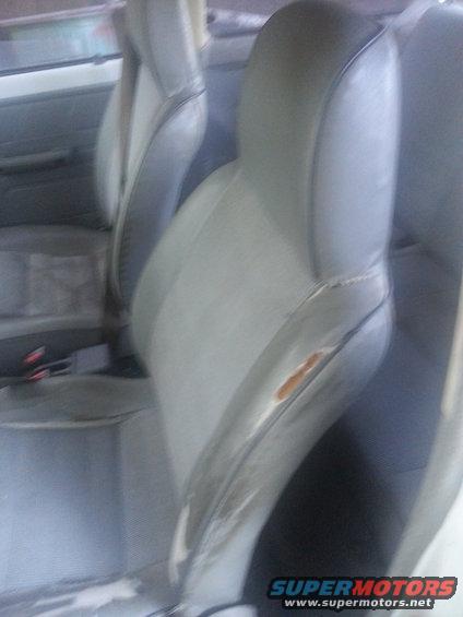 Car interior with torn gray and beige seats, seatbelts visible
