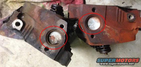 Two rusty engine cylinder heads with red circles around the combustion chambers